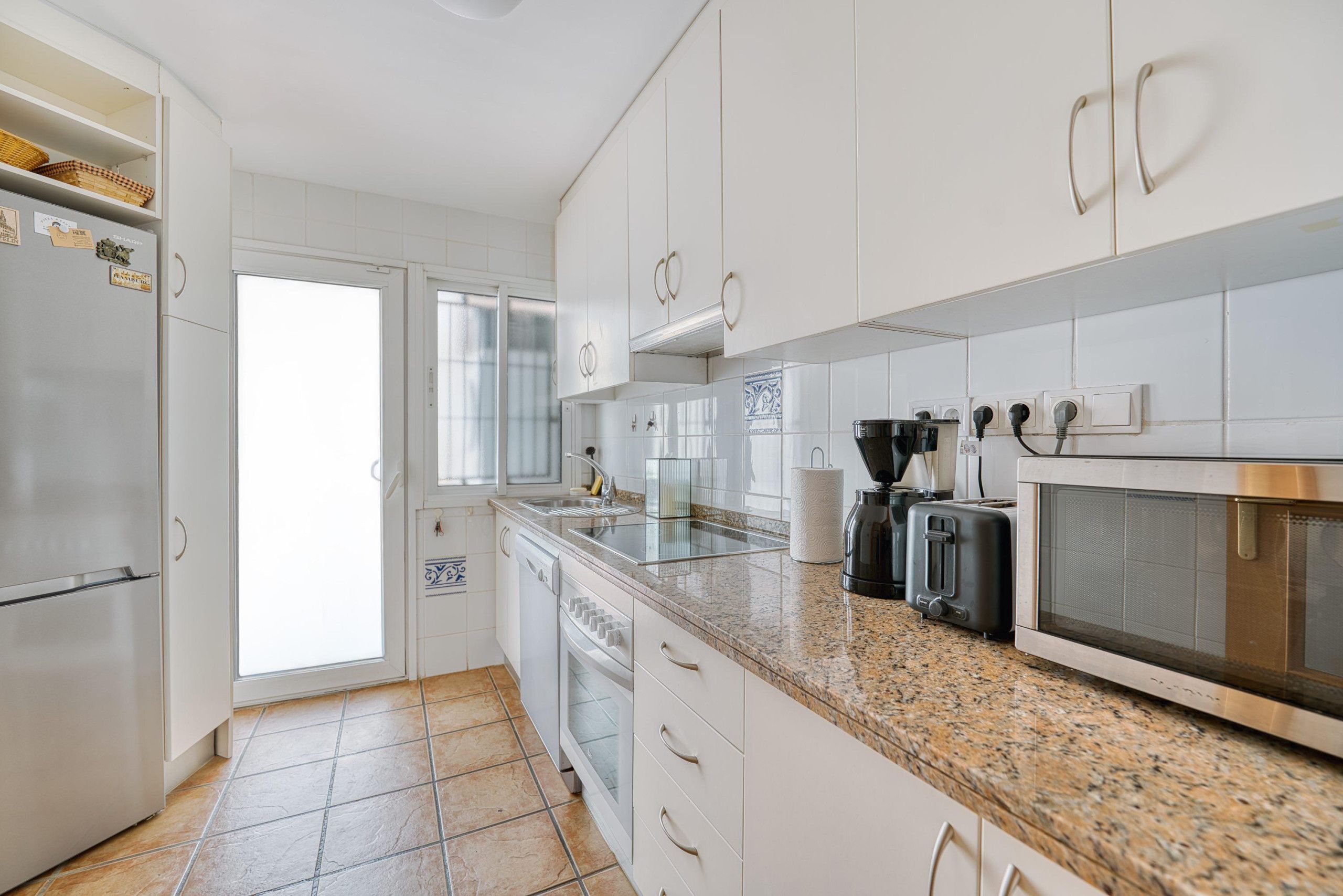 Een moderne keuken met witte kasten, een granieten aanrechtblad, roestvrijstalen apparatuur en een betegelde spatwand.