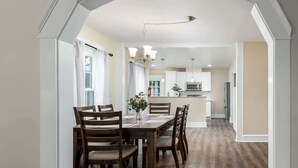 Een eetgedeelte met een houten tafel en stoelen, een vaas met bloemen en uitzicht op de keuken.