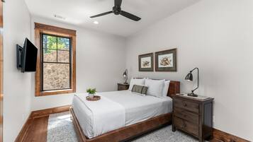 A bedroom with a bed, a nightstand, a TV mounted on the wall, and a window with a stone wall view.