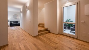 Un intérieur moderne avec un plancher en bois, un escalier et une grande porte-fenêtre coulissante donnant sur un espace extérieur aménagé avec du mobilier.