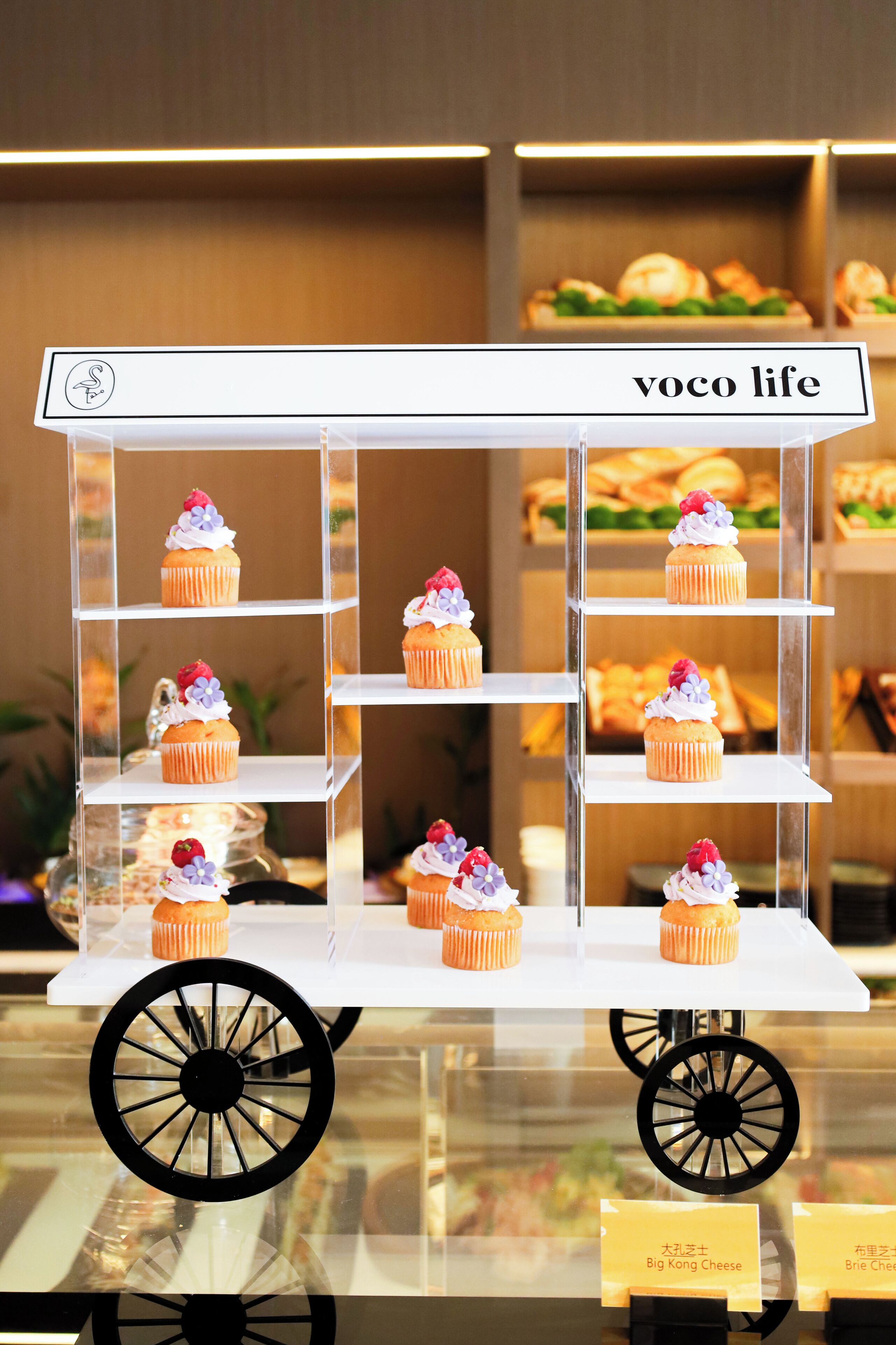 Eine Vitrine mit Cupcakes auf Regalen, beschriftet mit „voco life“.