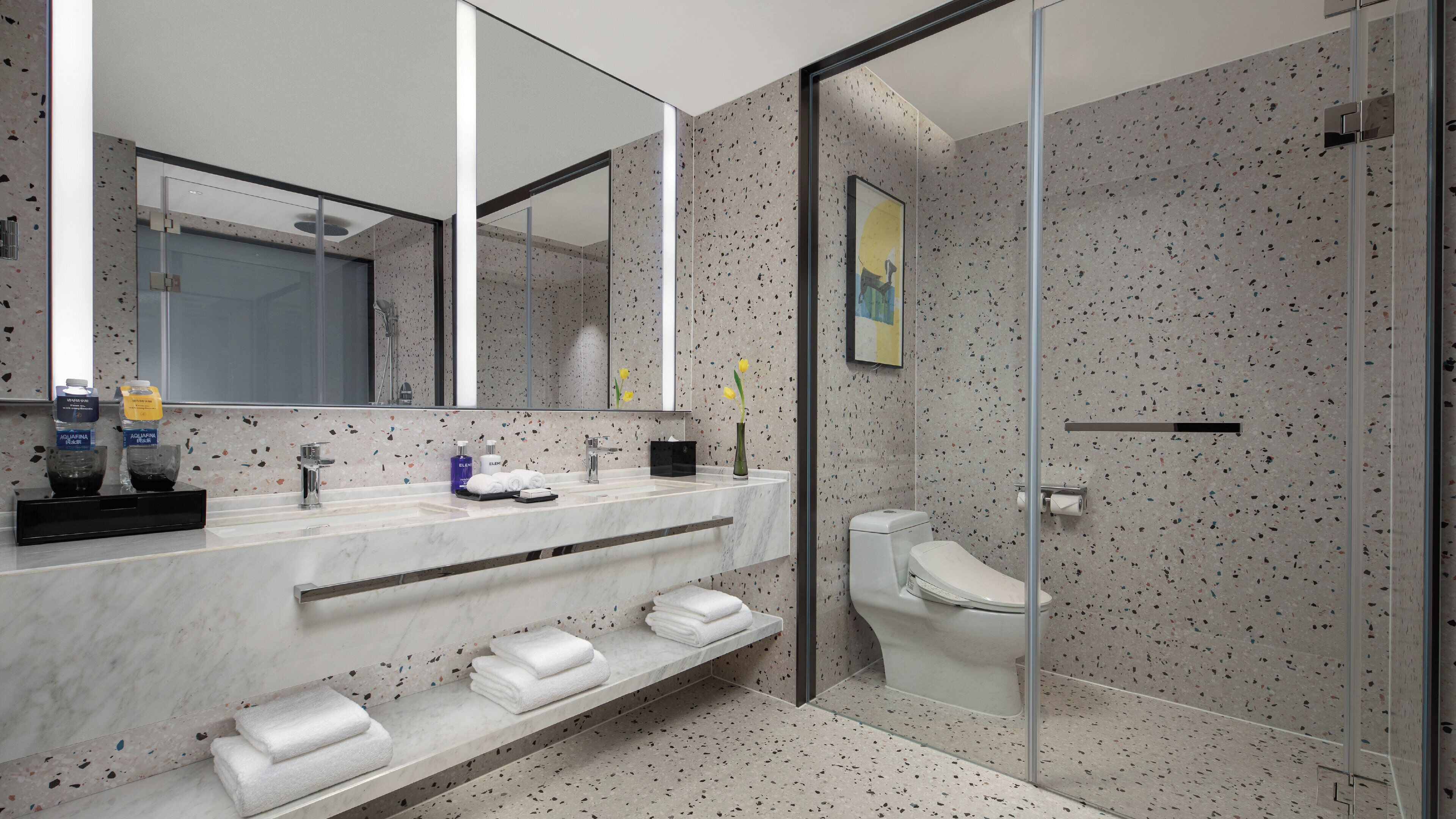 Un baño moderno con cabina de ducha de vidrio, tocador de mármol y un espejo grande.