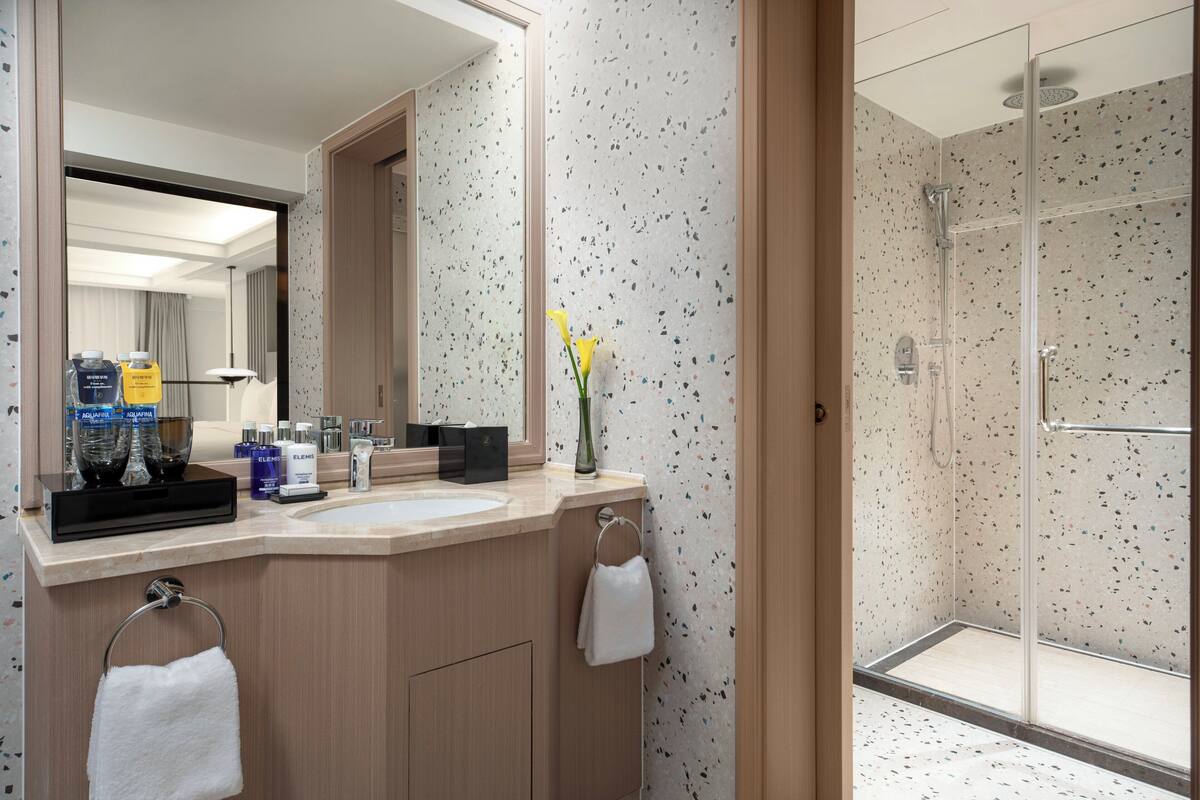 A modern bathroom with a shower, a sink with toiletries, and a mirror.
