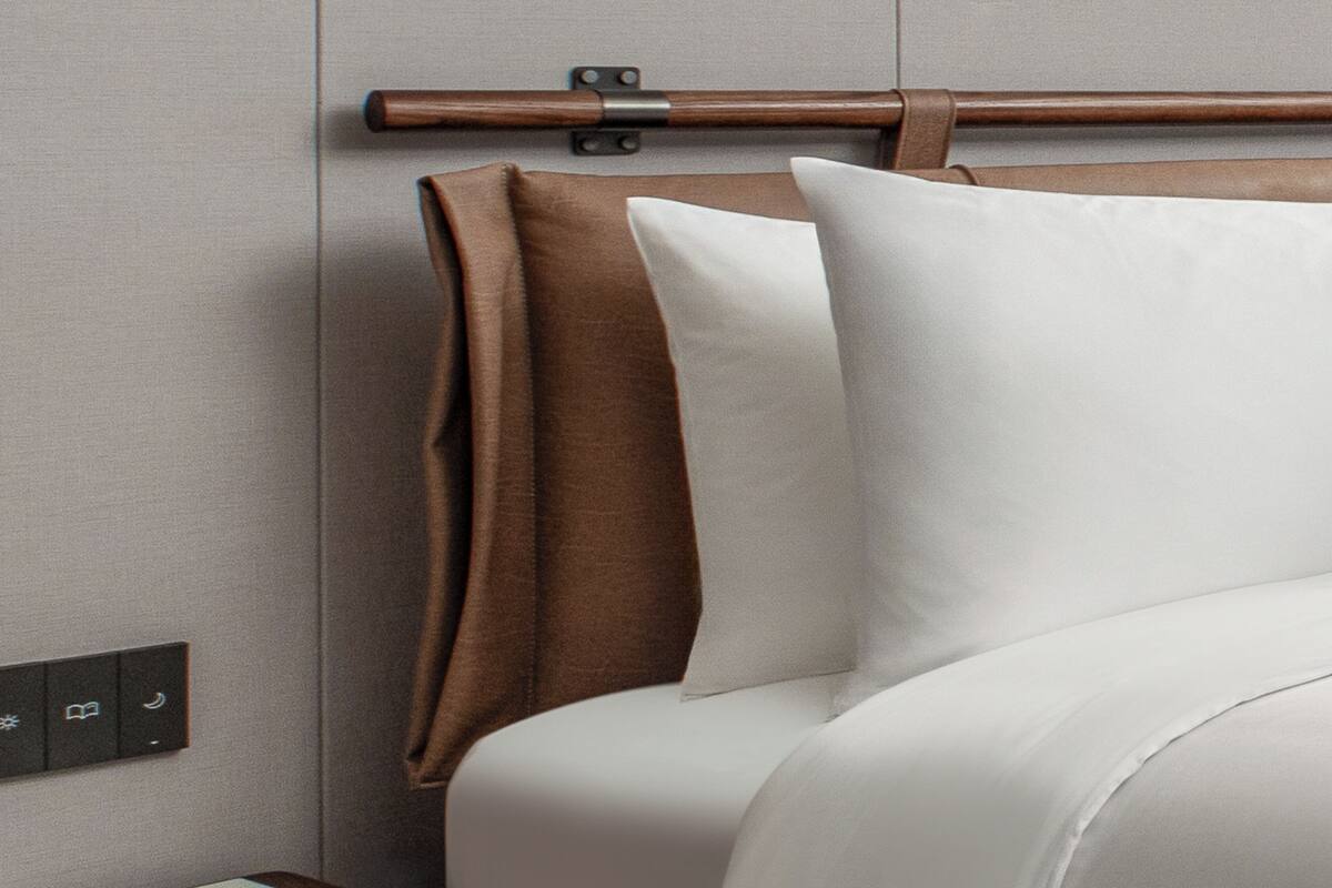 A bed with a wooden headboard, a brown accent pillow, and a white pillow.
