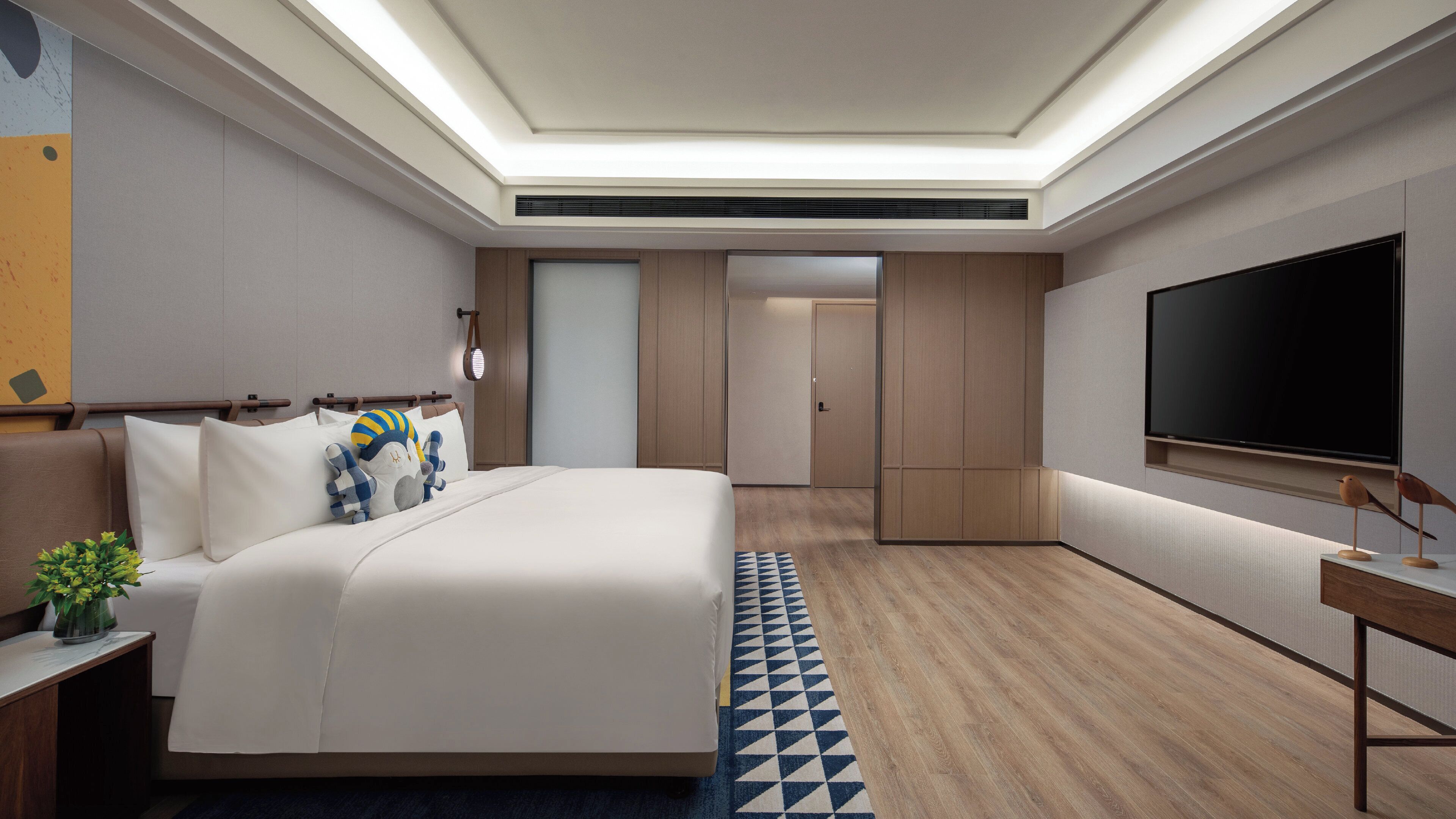 A modern hotel room with a large bed, a flat-screen TV, a desk, and a wardrobe.