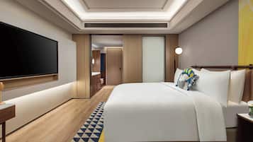 A modern hotel room with a large flat-screen TV, a neatly made bed, and a wooden floor.