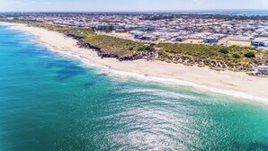 Luftaufnahme einer Küstenstadt mit Strand, Wohnhäusern und blauem Meer.