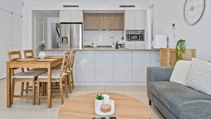Eine moderne Küche mit weißen Schränken, einer eingebauten Mikrowelle und einem Kühlschrank. Es gibt einen Essbereich mit einem Holztisch und Stühlen, sowie ein graues Sofa mit einem weißen Zierkissen.