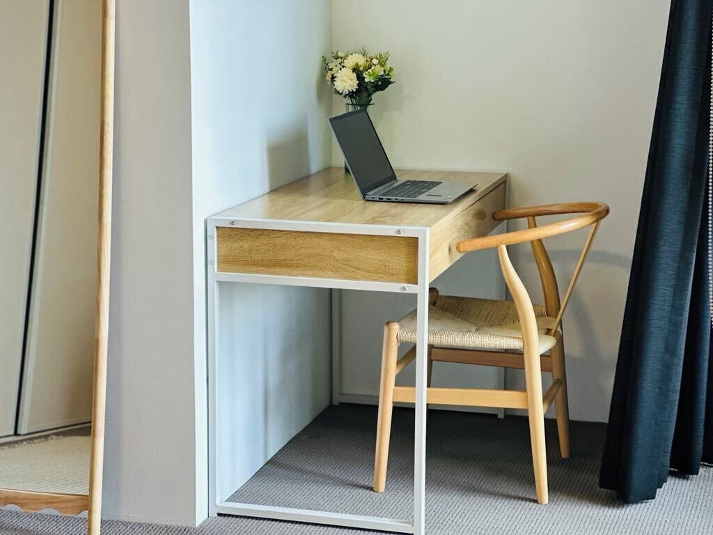 Un espace de travail compact comprenant un bureau et une chaise en bois, un ordinateur portable et un vase avec des fleurs.