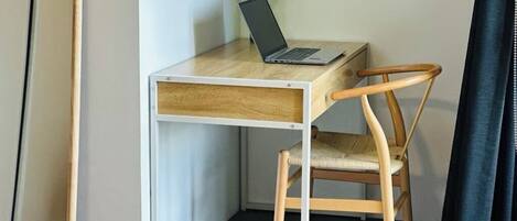 Un espace de travail compact comprenant un bureau et une chaise en bois, un ordinateur portable et un vase avec des fleurs.