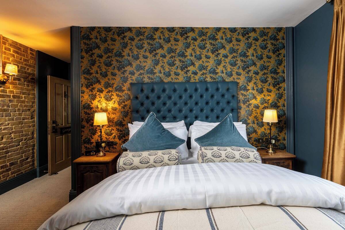 Una habitación de hotel con una cama grande, un cabecero capitonado, papel tapiz estampado y dos lámparas de noche.
