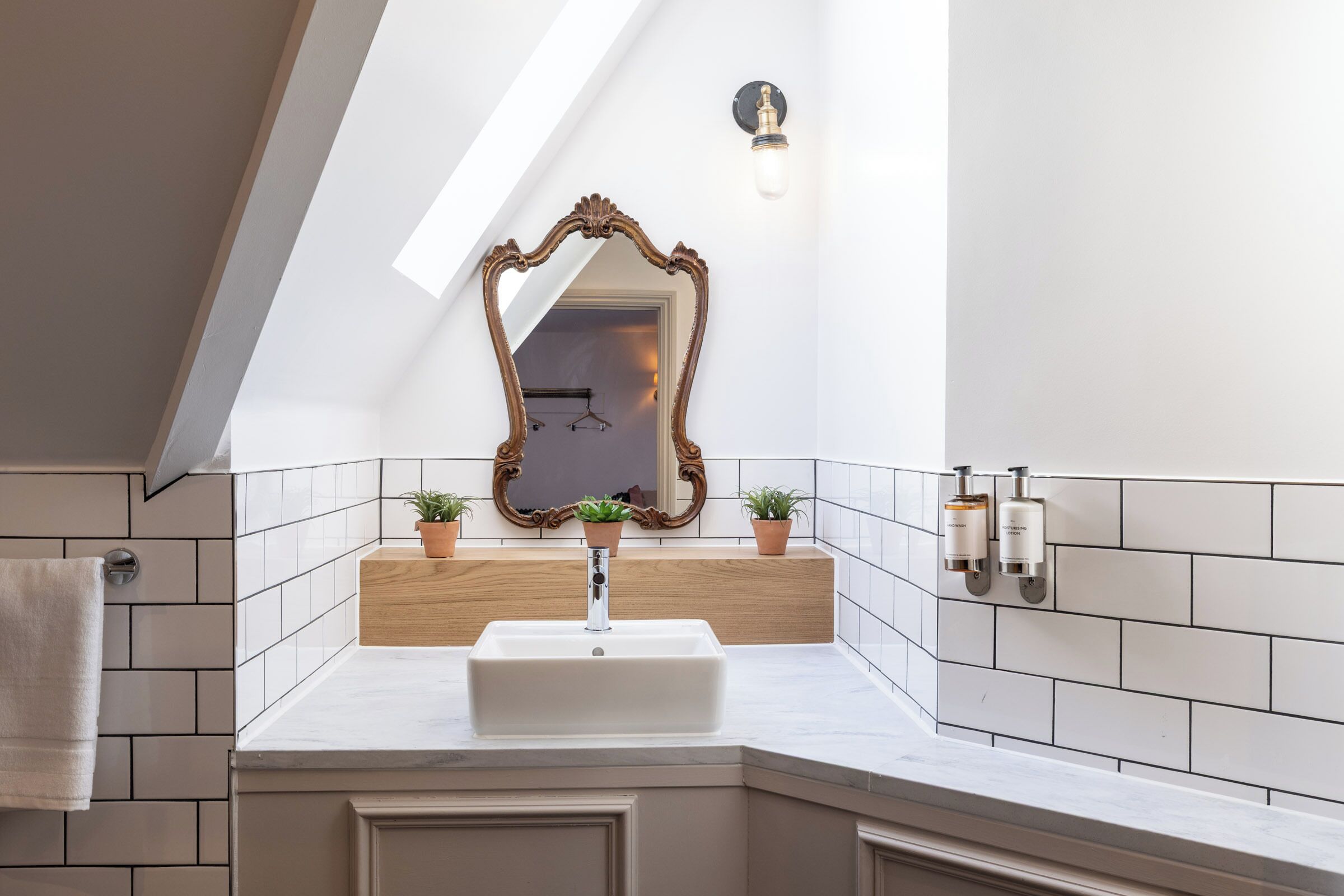 A bathroom with a white sink, a wooden vanity, a mirror with an ornate frame, and two potted plants.