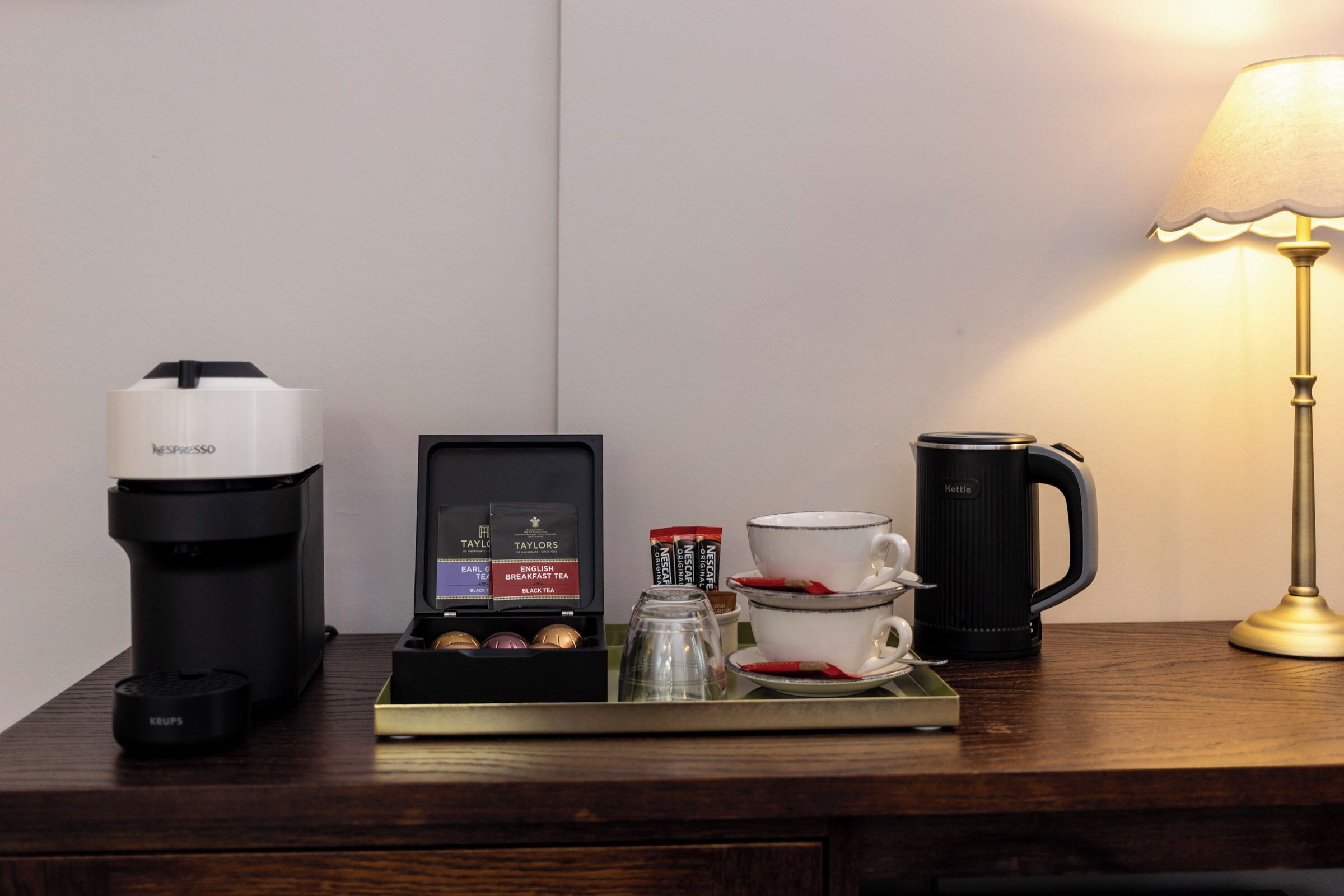 A coffee maker, a tea maker, a mug, a cup, and a lamp on a wooden surface.