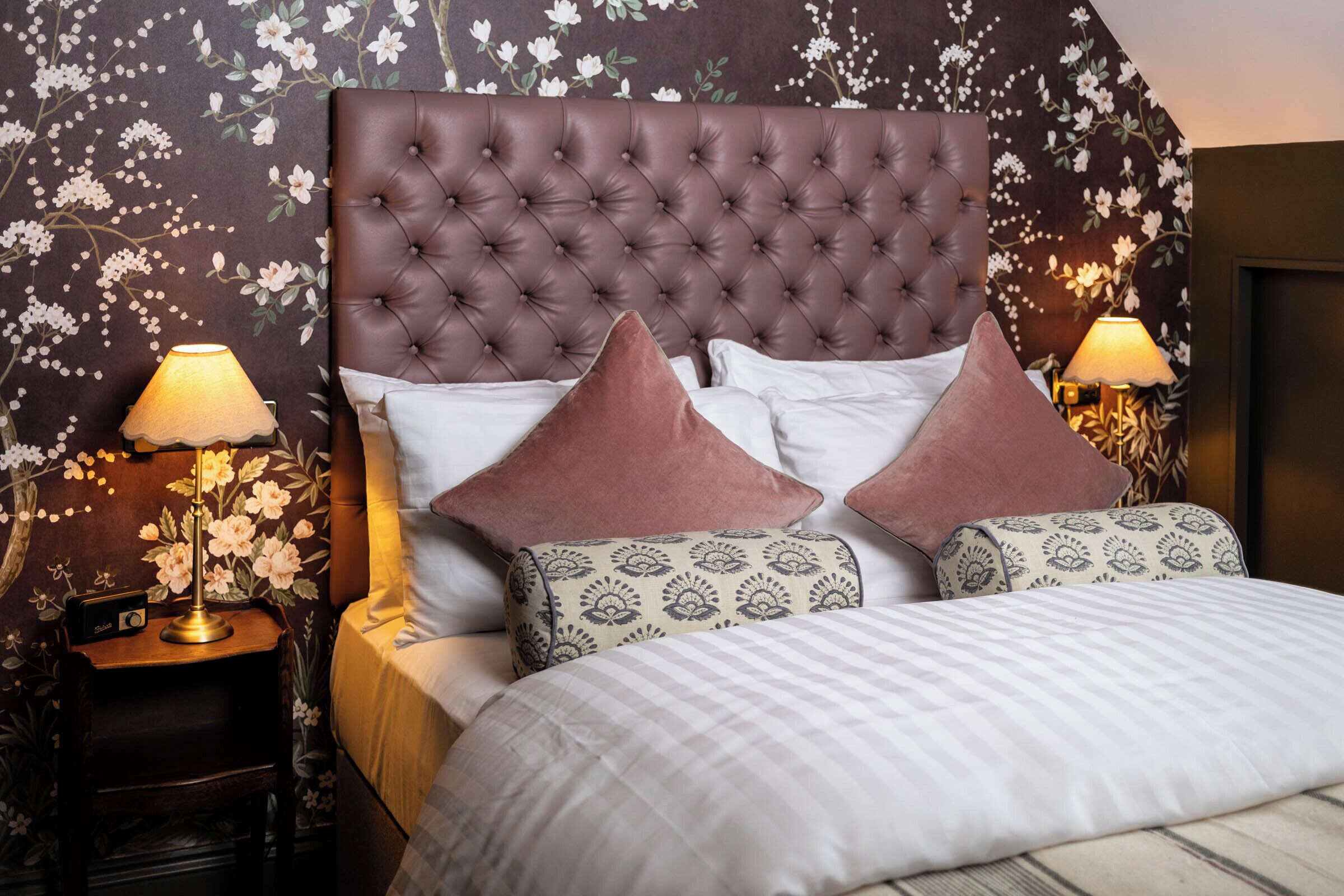 A bedroom with a tufted headboard, two bedside lamps, patterned pillows, and a striped bedspread.