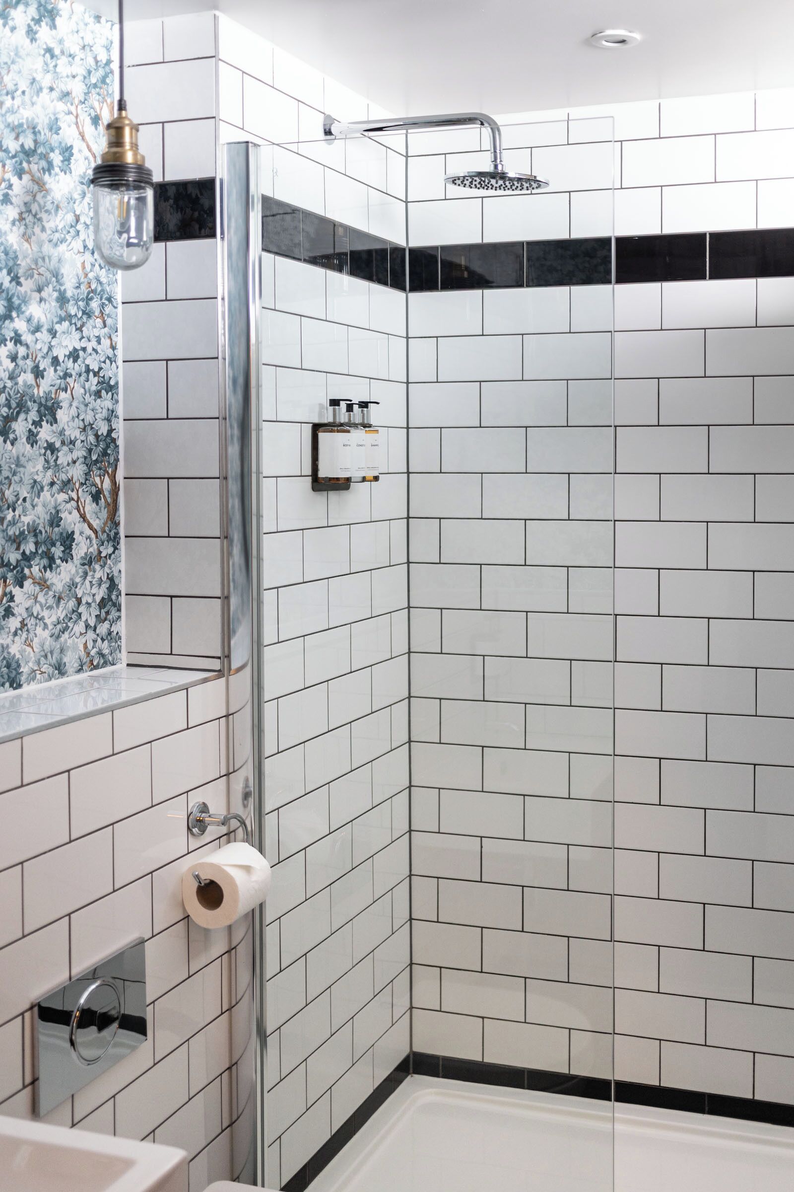A modern bathroom with white subway tiles, a glass shower enclosure, a toilet paper holder, and a towel rack.