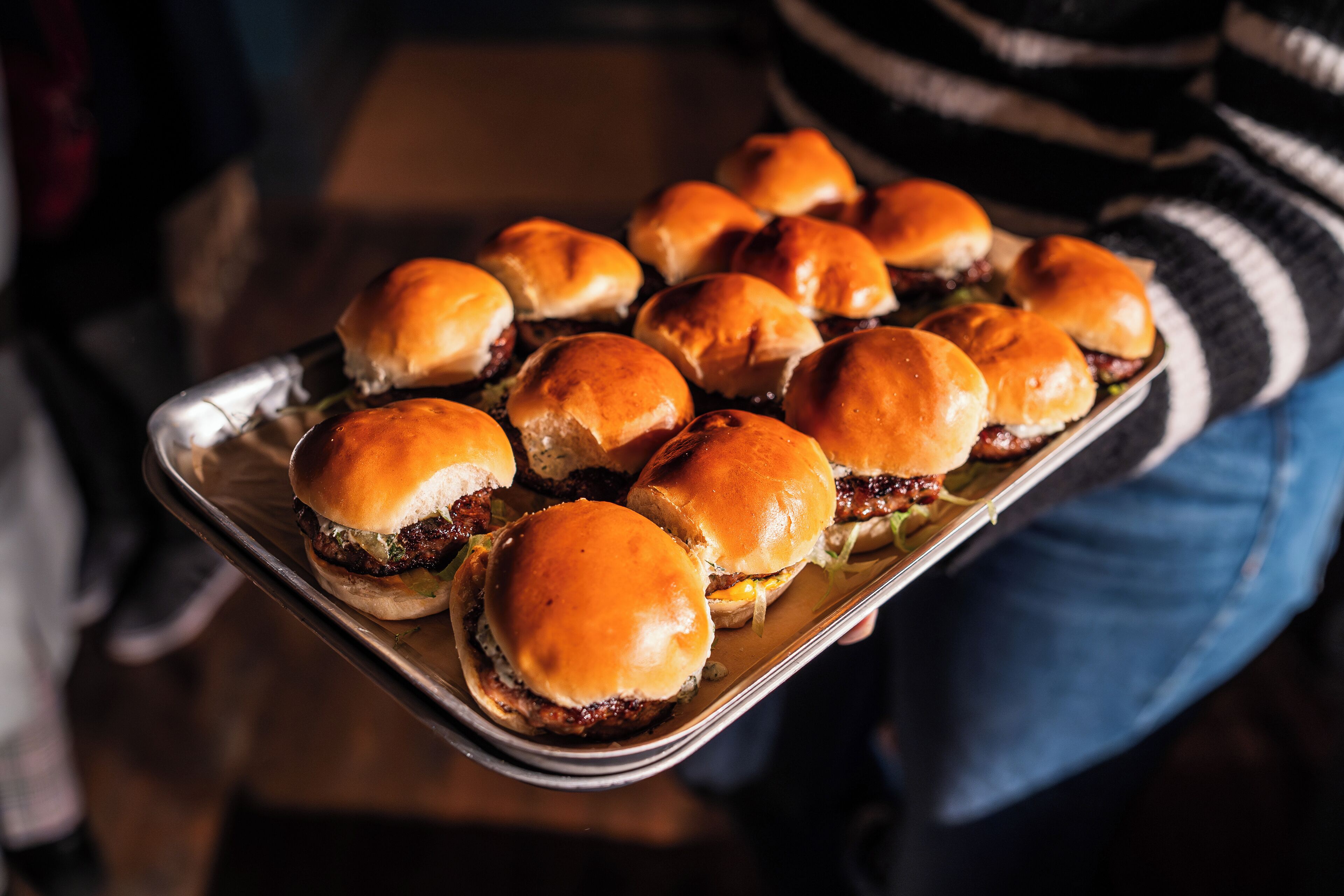 Een dienblad met burgers en broodjes, vastgehouden door iemand.