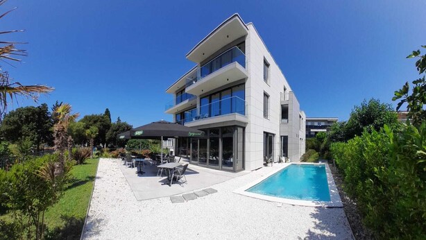 Een modern gebouw met twee verdiepingen, een zwembad, terras en een verzorgde tuin.
