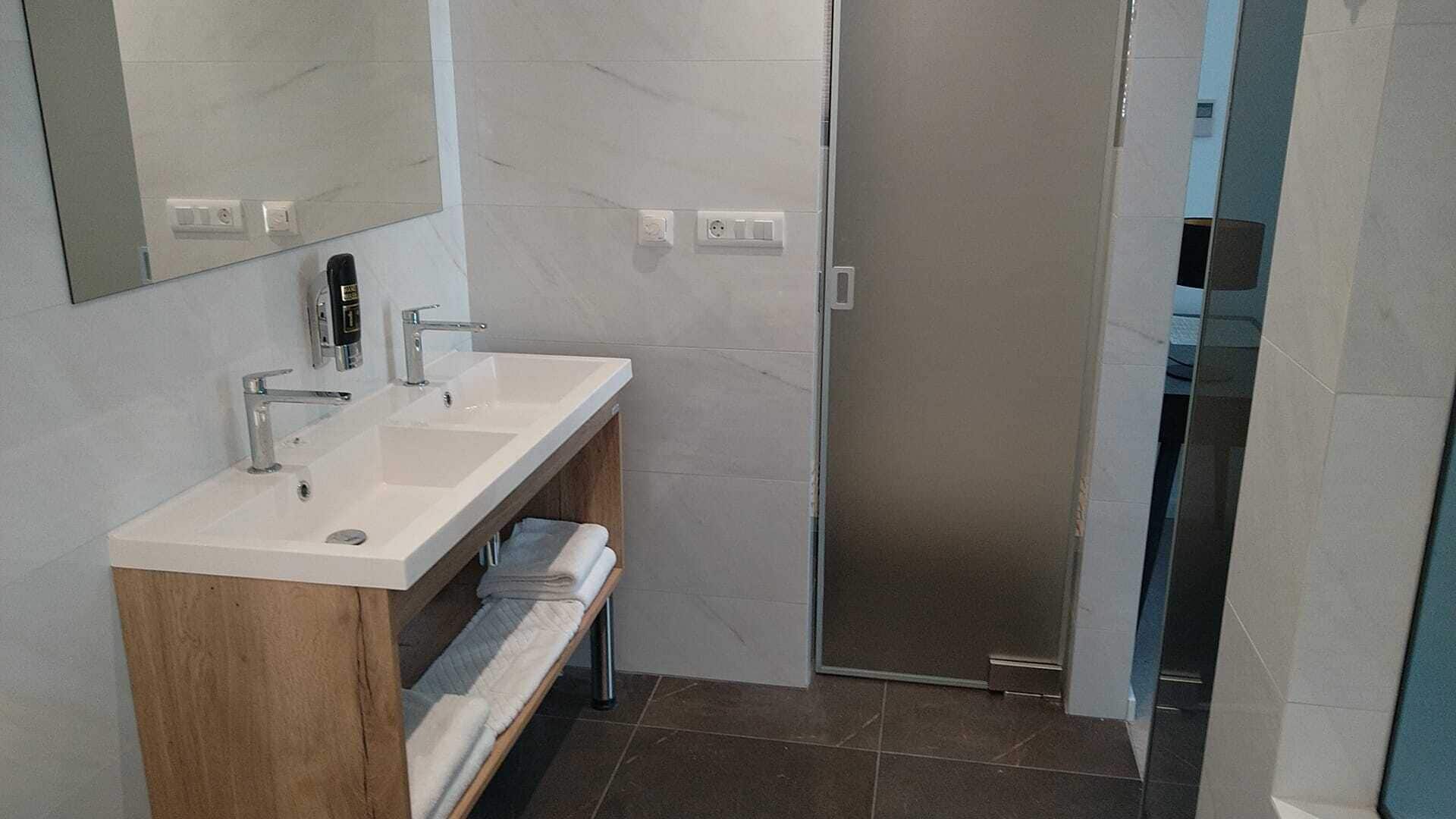 Un baño moderno con lavamanos doble, un espejo y zona de ducha.