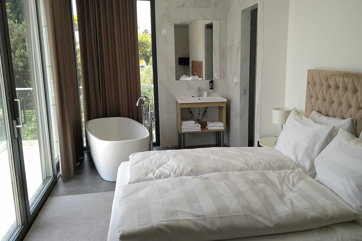 A hotel room with a large bed, a bathtub, a sink, and a mirror.