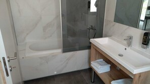 A modern bathroom with a marble floor, a bathtub, a glass shower enclosure, a white sink, and a wooden vanity. - HotelOscar (Kastela)