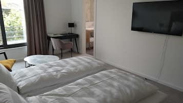 Una habitación de hotel con cama, escritorio, silla, televisor y ventana con cortinas.