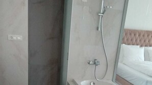 Een moderne badkamer met een vrijstaand bad, een douchecabine met glazen wanden en een grote spiegel die een bed met een gestapeld hoofdeinde weerspiegelt.