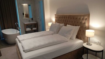 Ein Hotelzimmer mit einem großen Bett, zwei Nachttischen, einer Badewanne, einem Schminktisch mit Spiegel und einer Wandlampe.