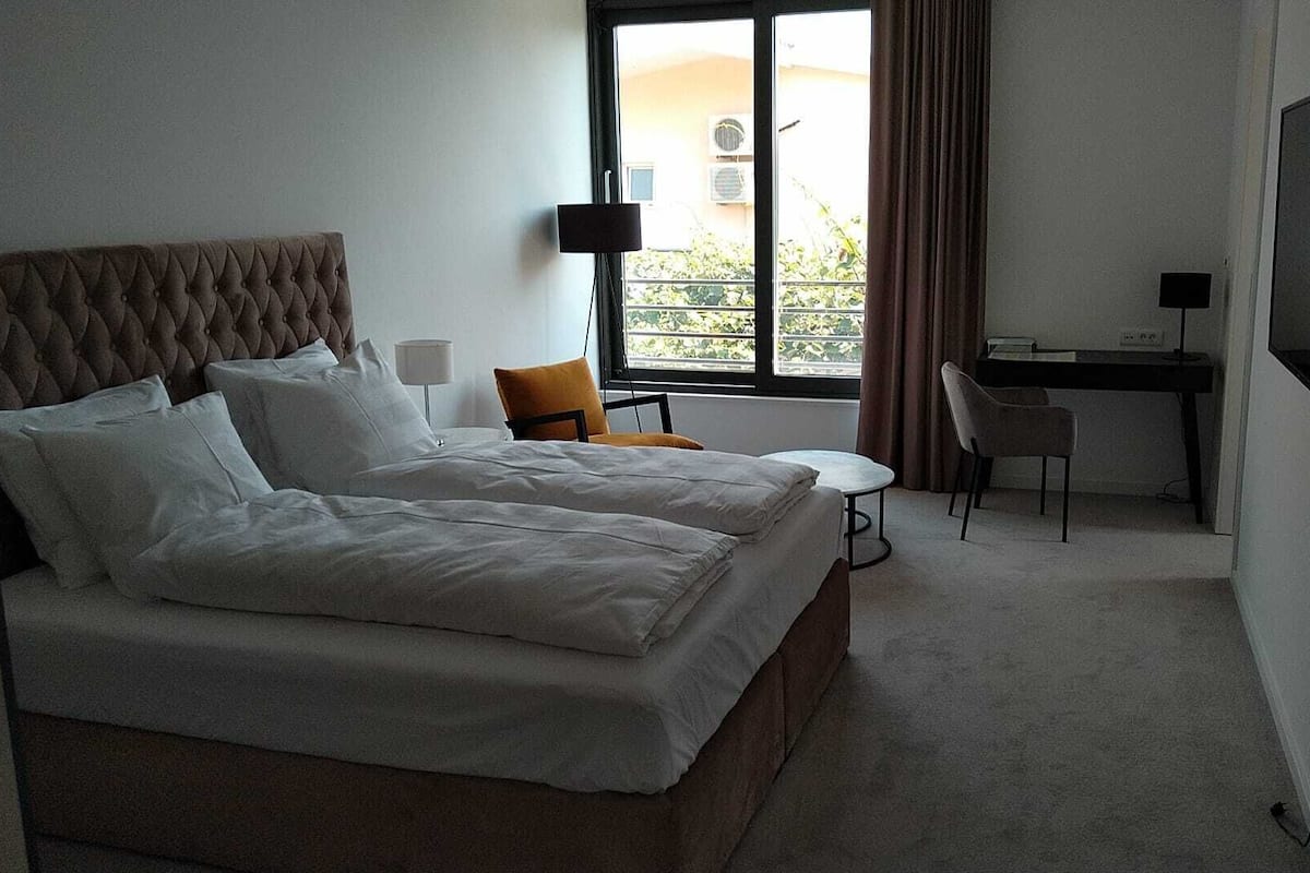 A hotel room with a large bed, a desk, a chair, and a TV.
