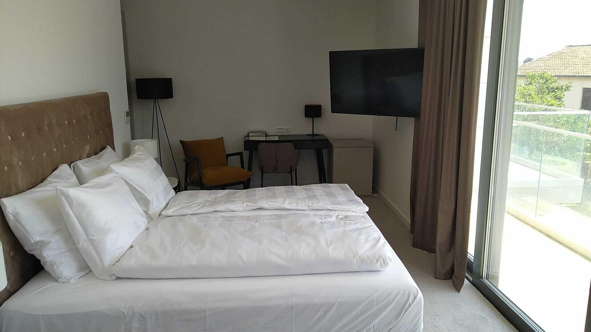 A hotel room with a large bed, a desk, a chair, a TV, and a window with a view of the outdoors.