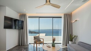 A modern living room with a large TV, a round coffee table, a sofa, a chair, and a view of the sea. - Astelia Villa • Heated Infinity Pool (Chania)