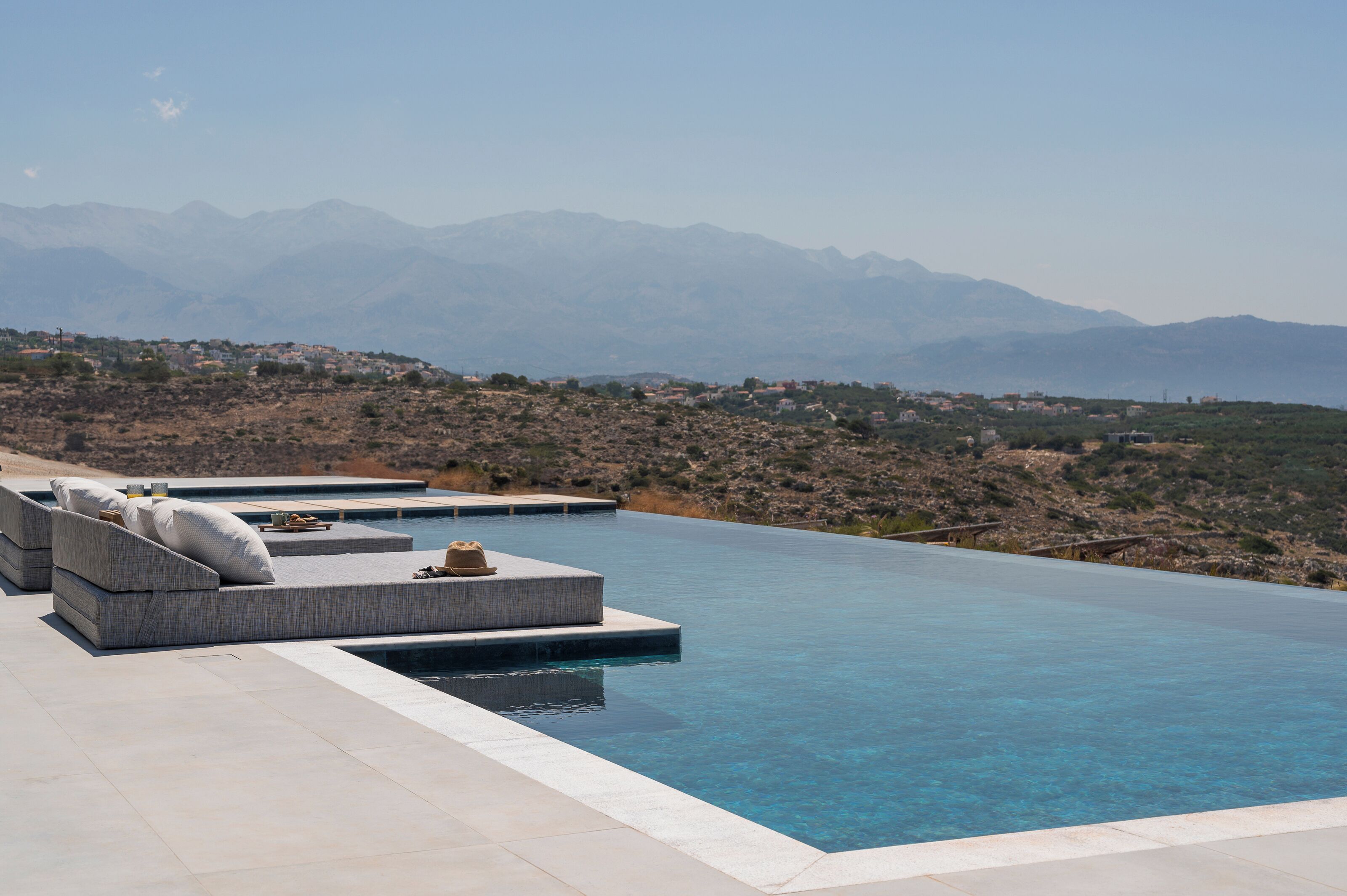 A modern infinity pool with built-in seating and a view of distant mountains.