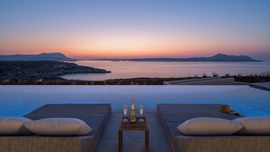 An infinity pool with a sunset view, two lounge chairs, and a table with a bottle and glasses. - Astelia Villa • Heated Infinity Pool (Chania)
