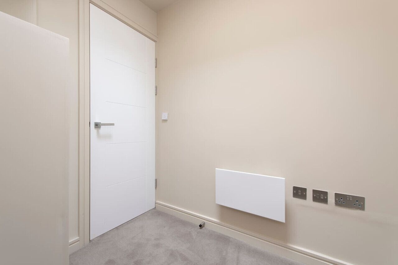 A room with a white door, a white wall-mounted panel, and three electrical outlets.