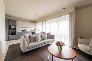 A modern living room with a sofa, a coffee table, and a kitchen in the background. - Chigwell 1BR + Study Escape (Essex)