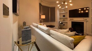 Een moderne woonkamer met een bank, een rond bijzettafeltje, een televisie en een open haard.