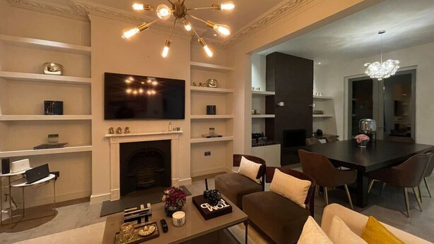 Een moderne woonkamer met een open haard, een eethoek en een aan de muur bevestigde televisie.