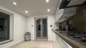 Een moderne keuken met een roestvrijstalen afzuigkap, een afvalbak en een glazen deur naar een andere kamer.