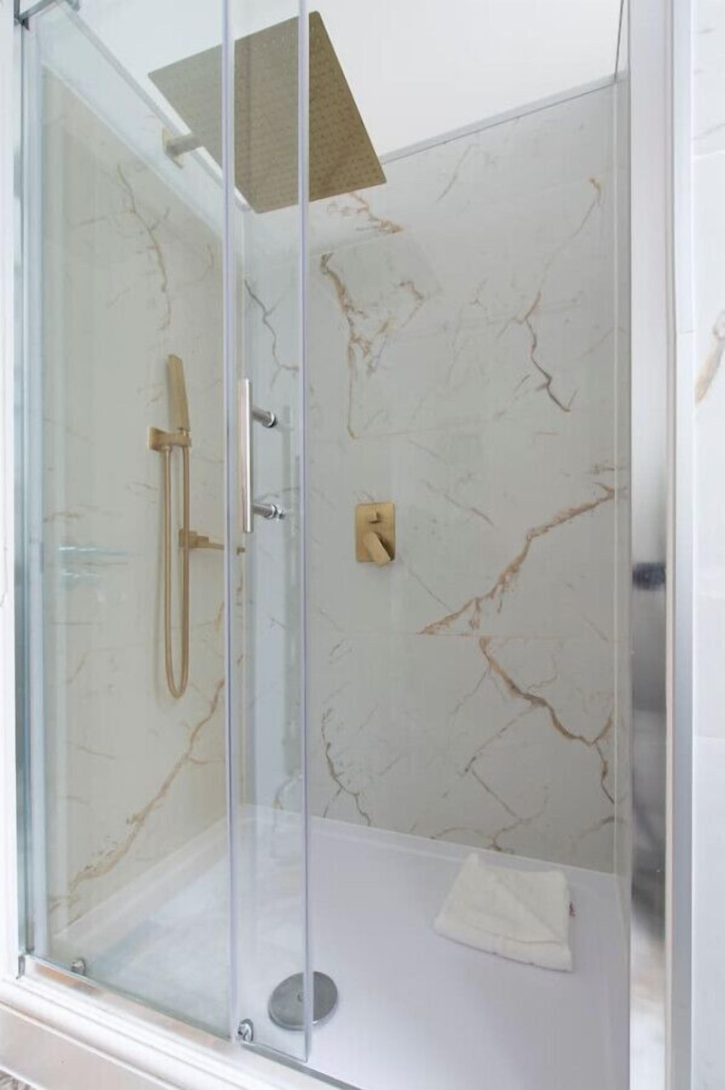 Une douche fermée par des parois de verre, avec un mur en marbre, une douchette à main et un panneau de commande.