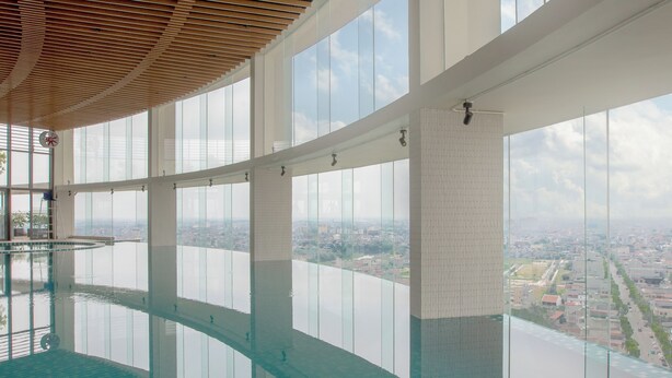 A high-rise building with a large indoor swimming pool, large windows, and a view of a cityscape. - Mandala Hotel & Suites Hai Duong (Hai Phong)