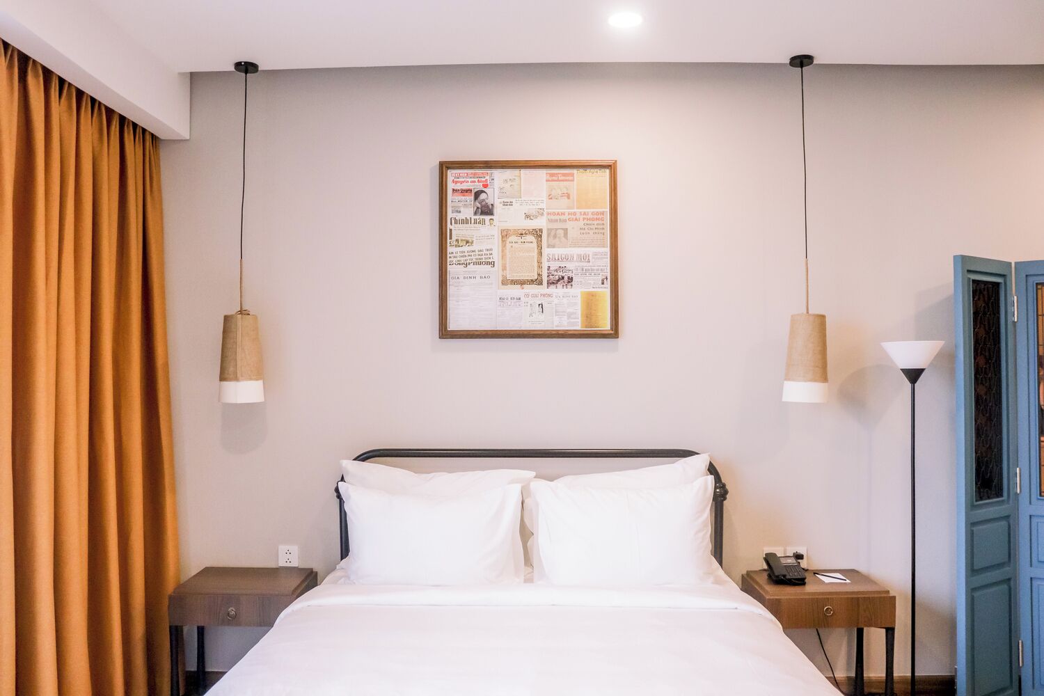 A hotel room with a bed, a nightstand, a lamp, a framed poster on the wall, and a blue door.