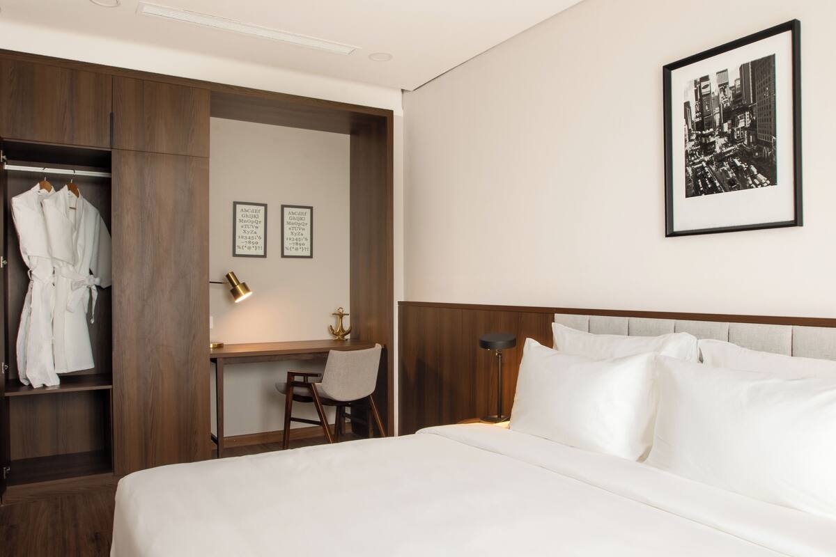 Habitación de hotel con cama, escritorio, silla, armario y un cuadro en la pared.