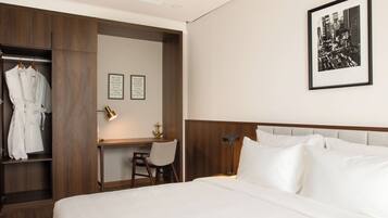 A hotel room with a bed, a desk, a chair, a wardrobe, and a framed picture on the wall.