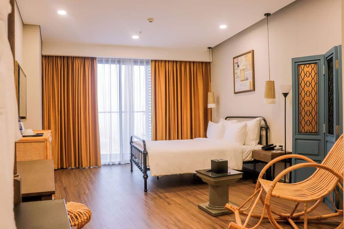 Habitación de hotel con cama, escritorio, silla, lámpara y ventana con cortinas.