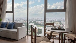 A modern living room with a large window offering a city view, a sofa with cushions, and a round table with a tray. - Mandala Hotel & Suites Hai Duong (Hai Phong)