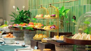A buffet with various food items and a decorative plant in the background. - Mandala Hotel & Suites Hai Duong (Hai Phong)