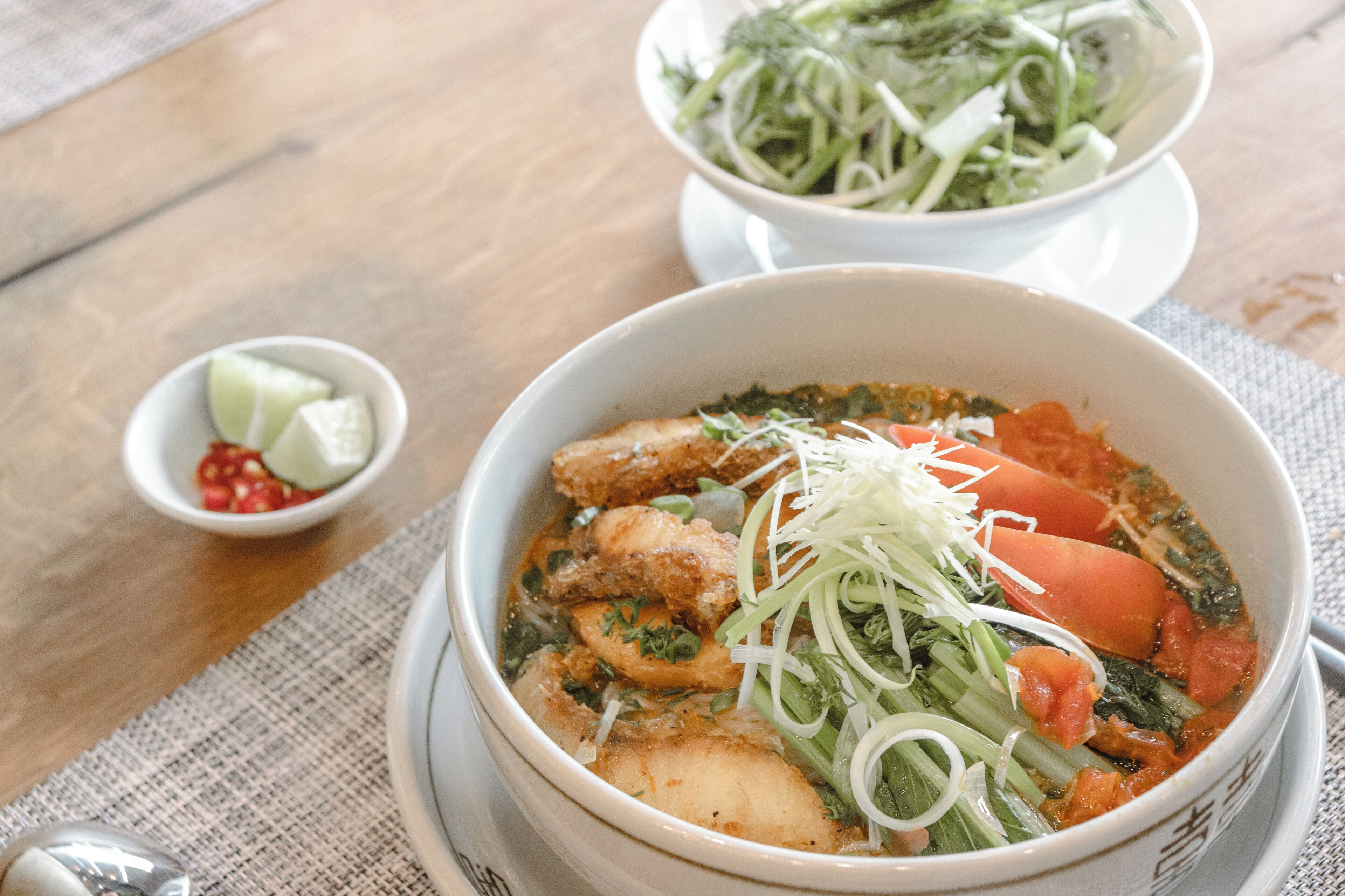 Un bol de soupe aux légumes et à la viande, un petit bol de chili et une assiette de nouilles.