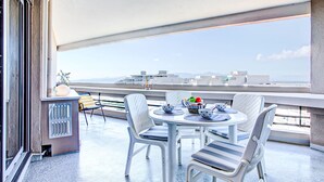 A balcony with a round table, white chairs, and a view of the sea.