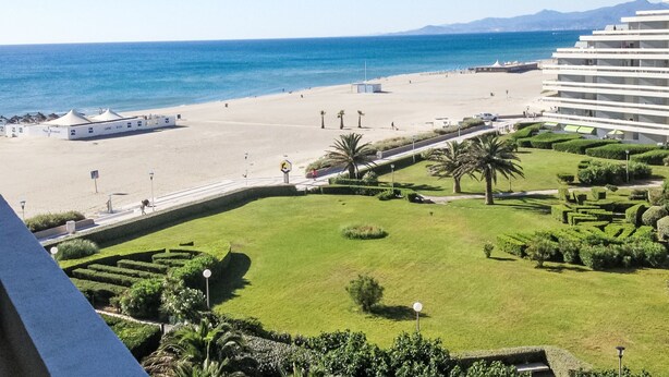 A beach view with a hotel, a sandy beach, and a clear blue sky.