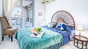 A bedroom with a bed, a chair, a table, and a balcony.