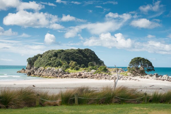A coastal landscape with a sandy beach, rocky outcrops, and dense greenery.